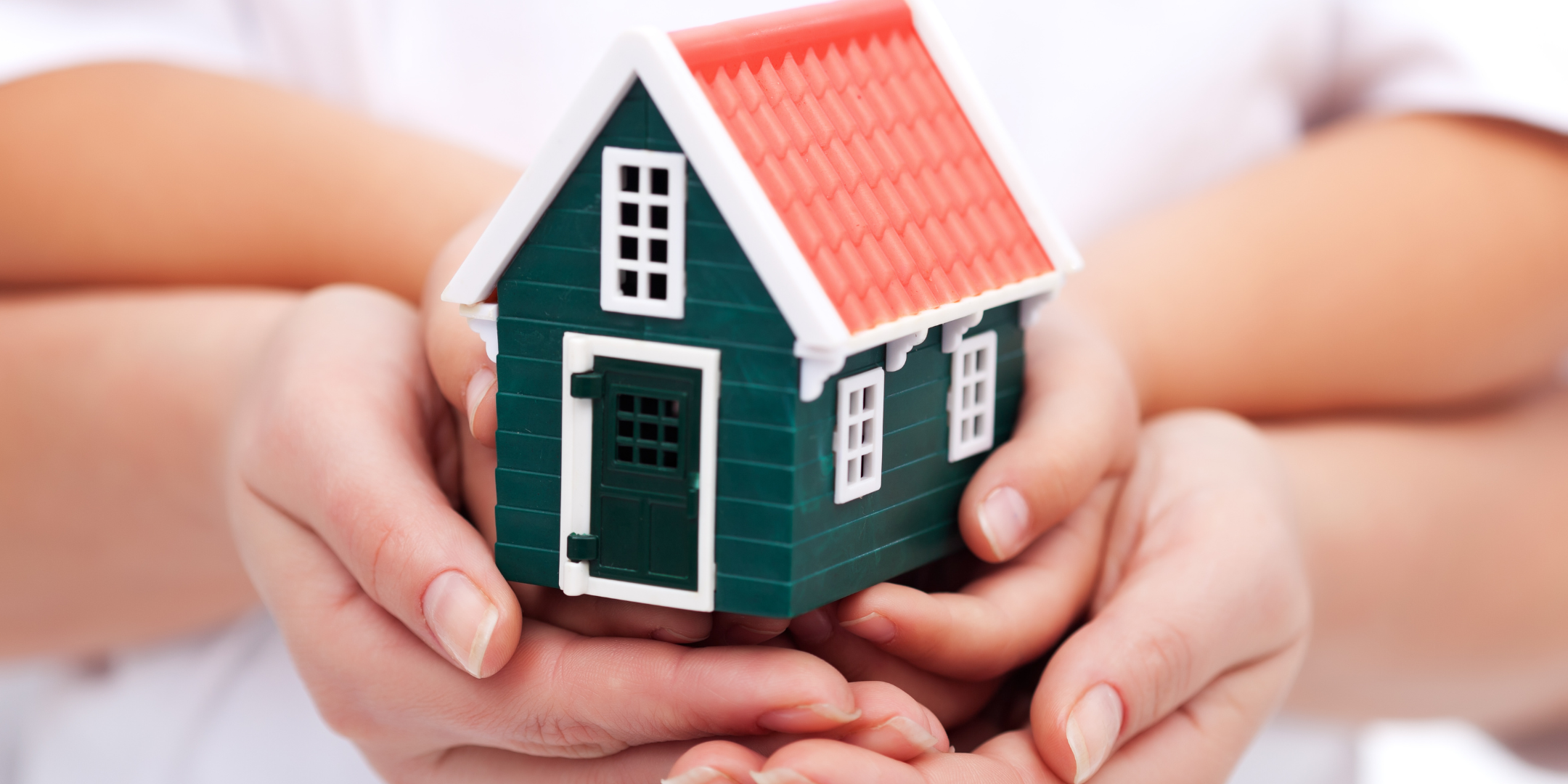 The hands of a family holding a toy home, symbolizing togetherness and comfort.